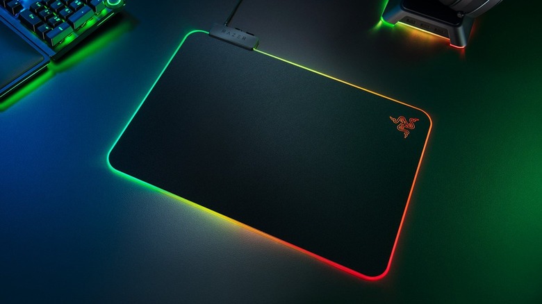 A black Razer Firefly V2 gaming mouse pad on a black desk with its edges lit up in multiple colors.