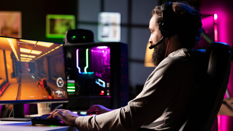 A bearded man wearing a headset and playing an FPS video game on a black gaming PC.