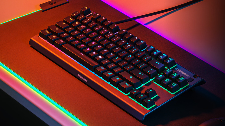A black SteelSeries Apex 3 TKL RGB gaming keyboard on a desk mat bathed in bright red light.
