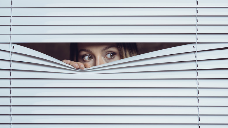 A woman peeking through blinds that are covering a window.