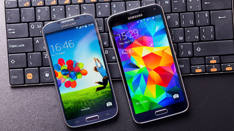 A Samsung Galaxy S4 and Galaxy S5 lying next to each other on top of a keyboard.