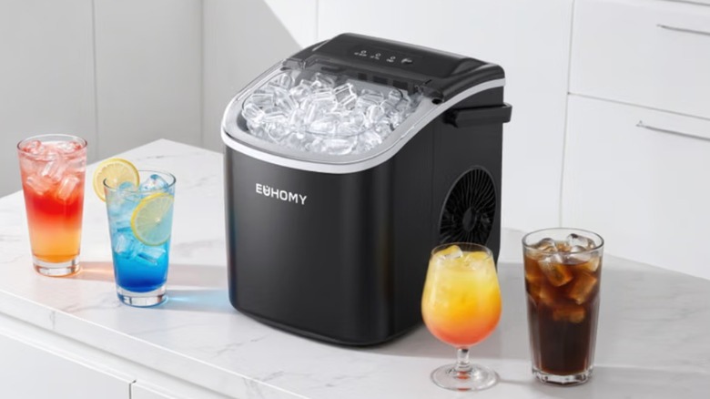 The Euhomy Dart H1 ice maker on a kitchen countertop beside some drinks.