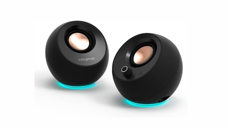 Two round orb-shaped speakers in black with a blue light coming out of the bottom of each. One of them has a volume knob and the other has "CREATIVE" written on it.