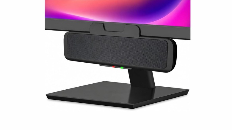 A black rectangular speaker bar clipped onto a monitor. There is a red and green light at the bottom.