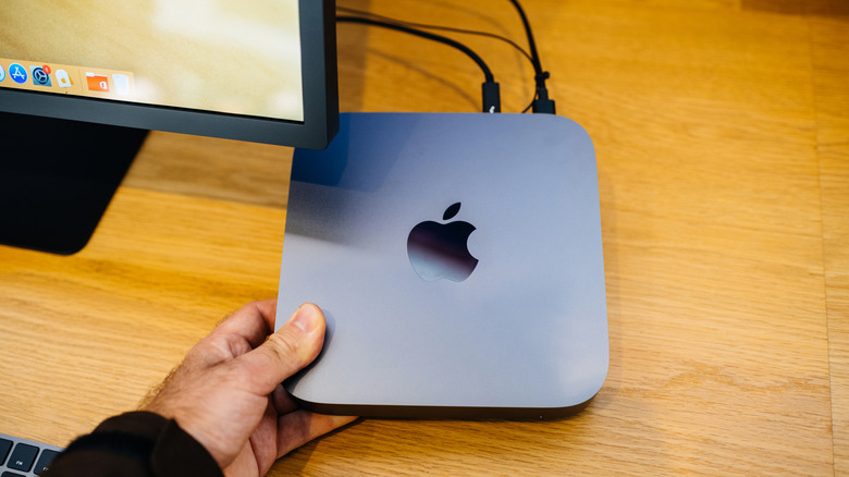 A person holds a Mac Mini under a computer monitor.