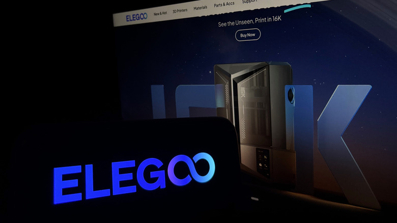 An Elegoo sign in front of a screen showing the company website.