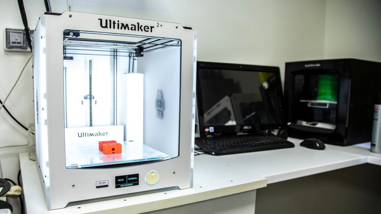 A white Ultimaker 3D printer on a desk next to a computer.