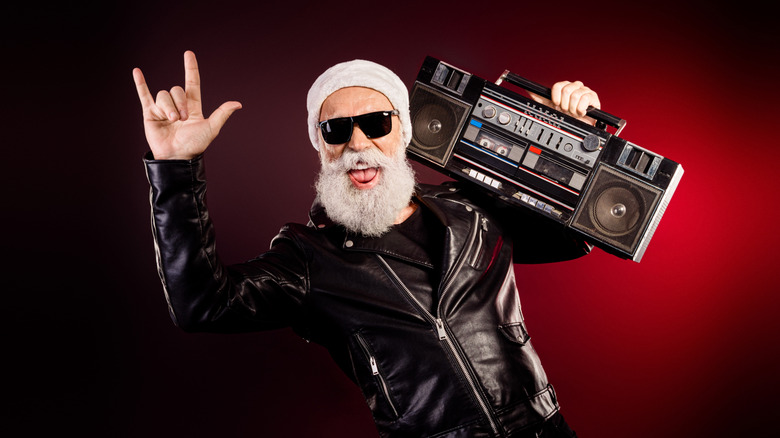 A man with a white beard holding a boombox on one shoulder and doing the horns sign with his other hand