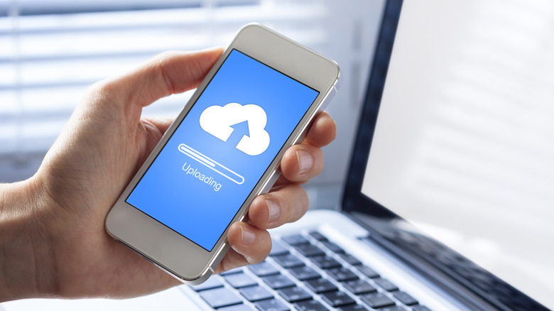 A person holding a phone with a cloud icon and message that says uploading.