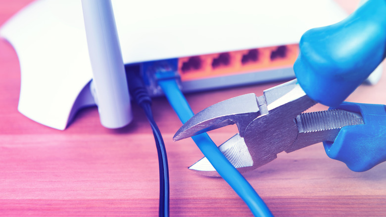A sidecutter about to cut through an Ethernet cable plugged into a router.