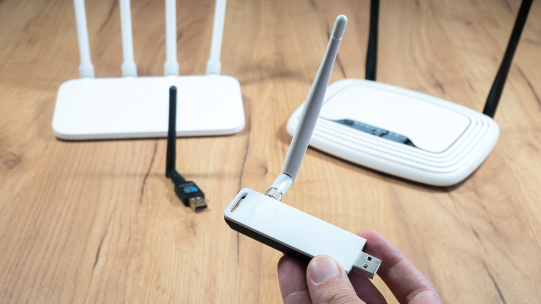 A USB Wi-Fi adapter with an external antenna shown alongside routers.
