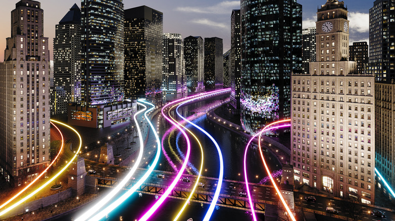 A cityscape at dusk, with vivid, multicolored light trails flowing along the roads and bridges like streams of data.