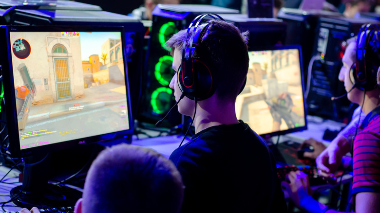 A group of gamers sitting at desktop PCs, wearing headsets and playing a fast-paced multiplayer shooter.