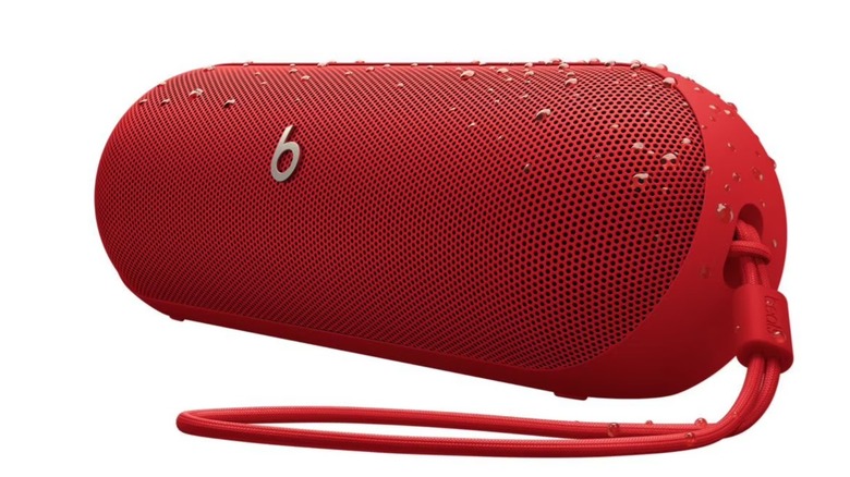 The Beats Pill Bluetooth speaker with its strap and water droplets on it, on a white background.