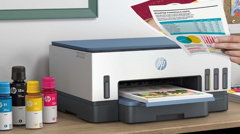 The HP Smart Tank 7002 all-in-one printer with ink bottles beside it, placed on a wooden surface.