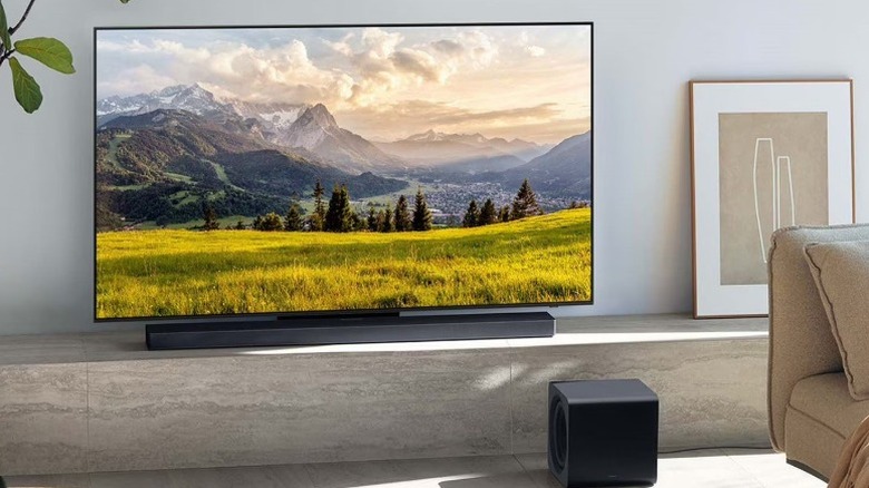 The Samsung HW-QS700F underneath a smart TV with the subwoofer placed near the couch.