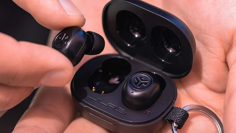 The JLab JBuds Mini wireless earbuds and their charging case on a person's hand.