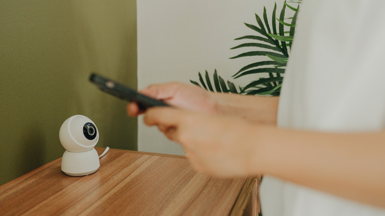 A person controlling the CCTV placed on a wooden surface with their phone