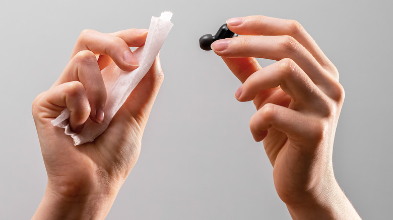 Two hands cleaning a wireless bud using a wet wipe.