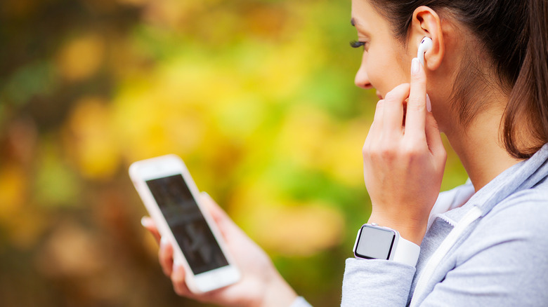 A woman adjusting her AirPods while looking at her phone screen.