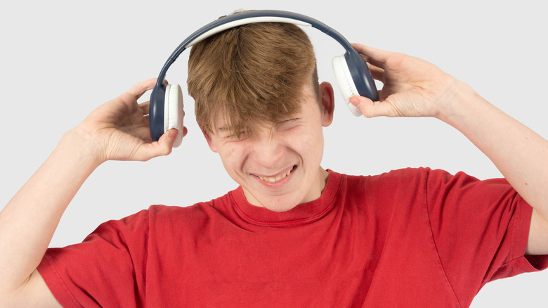 A young man grimacing and pulling his headphones off his ears.