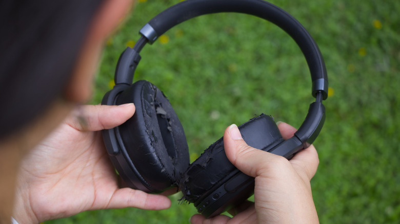 A person holding a set of headphones with worn earcups.