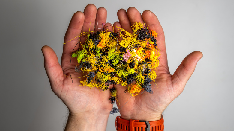 Two hands holding a tangled pile of colorful waste material from a 3D printer.