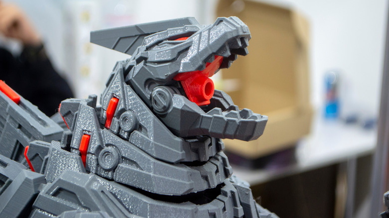 Close-up of a gray and red 3D-printed robotic dinosaur figure with its mouth open, showing detailed mechanical-style features.