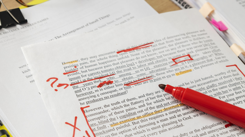 A marked-up printed document covered in red editing notes, highlights, and corrections, with a red marker pen resting on the page.