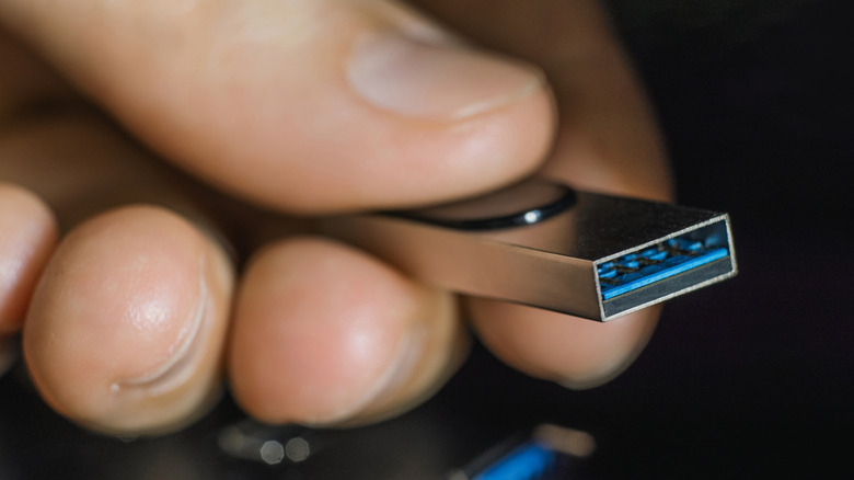 An extreme close-up of a hand holding a metal USB flash drive.