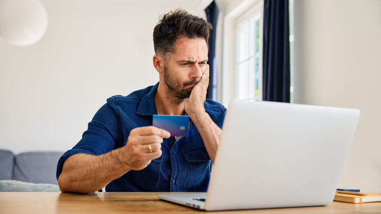 A person looking exasperated while online shopping on a laptop using their credit card.