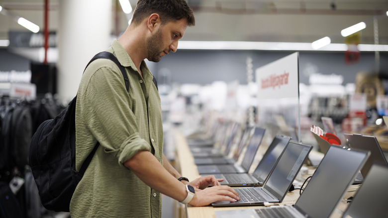 A man looking at laptops for sale in a store.