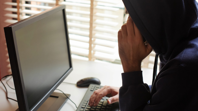 A person using a computer with their face hidden by a hoodie.