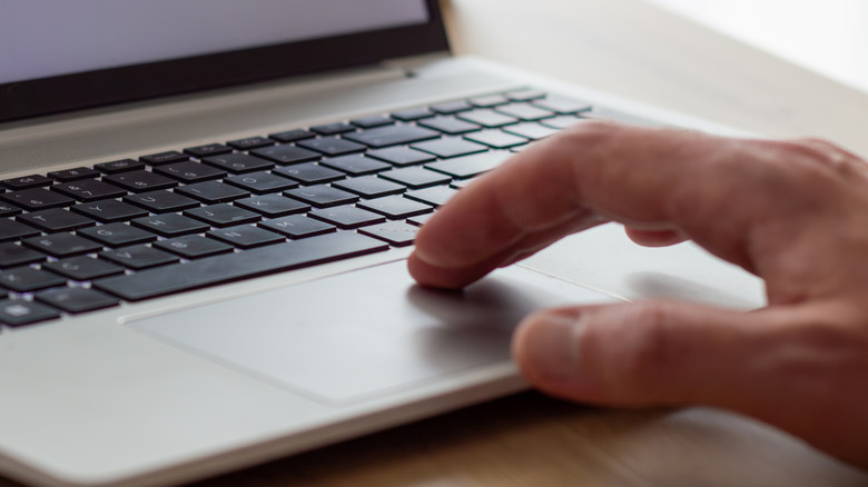 A hand touching a laptop touchpad