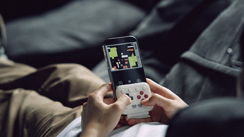 A person holding an iPhone playing a retro game with the 8Bitdo FlipPad controller attached to the phone.