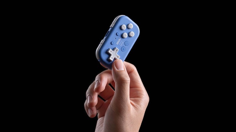 A person holding up the compact 8Bitdo Micro Gamepad.