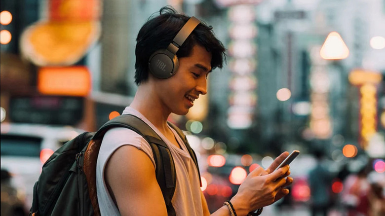 A person wearing the JBL Tune 660NC headphones and using their phone while walking in a city