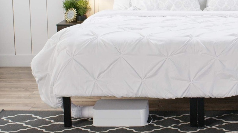 A BedJet device under a bed with a white comforter