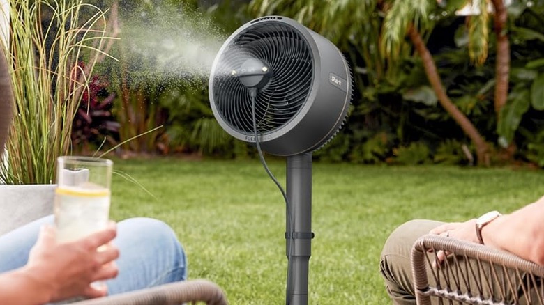 A Shark FlexBreeze Pro misting fan between two people sitting in chairs in a garden setting