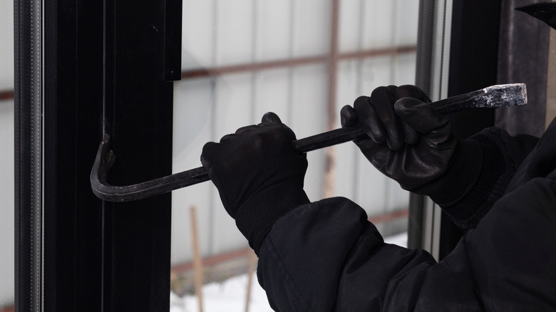 Close-up of a burglar using a crowbar to pry open a window frame.