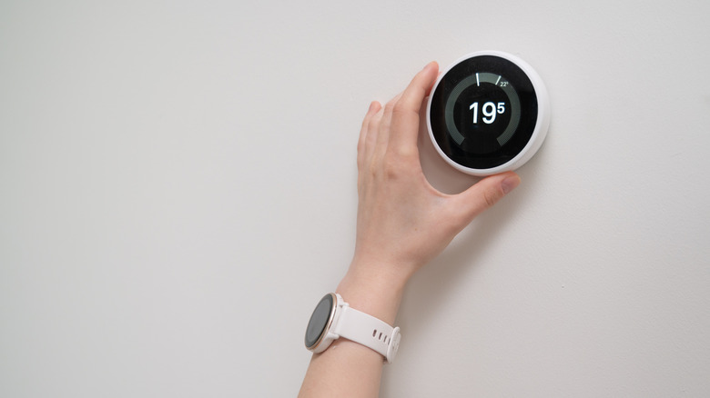 A hand adjusting a wall-mounted smart thermostat.