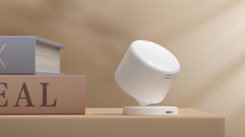 A compact smart environmental sensor that measures light levels, temperature, and humidity next to some books.