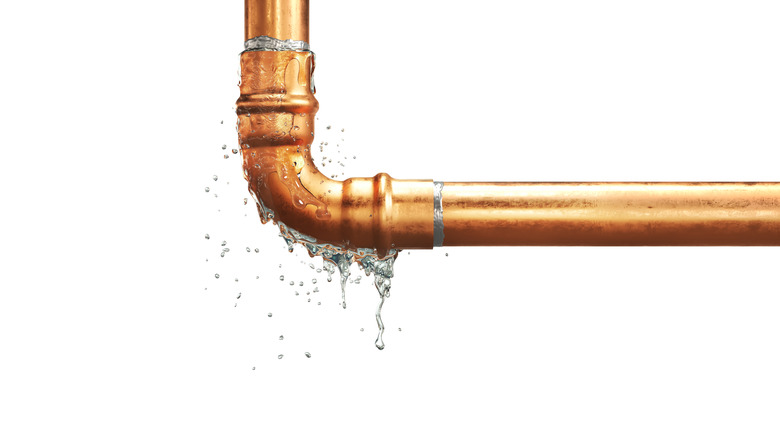 A leaking copper water pipe spraying water from an elbow joint.
