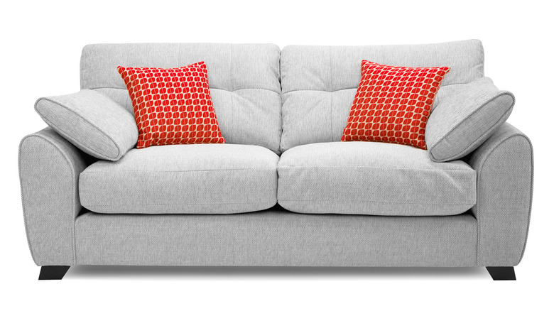 A light gray two-seat fabric sofa with oversized arm cushions and two red patterned throw pillows against a white background.