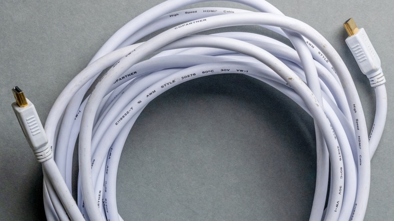 A coiled white HDMI cable with gold-plated HDMI connectors at both ends on a gray surface.