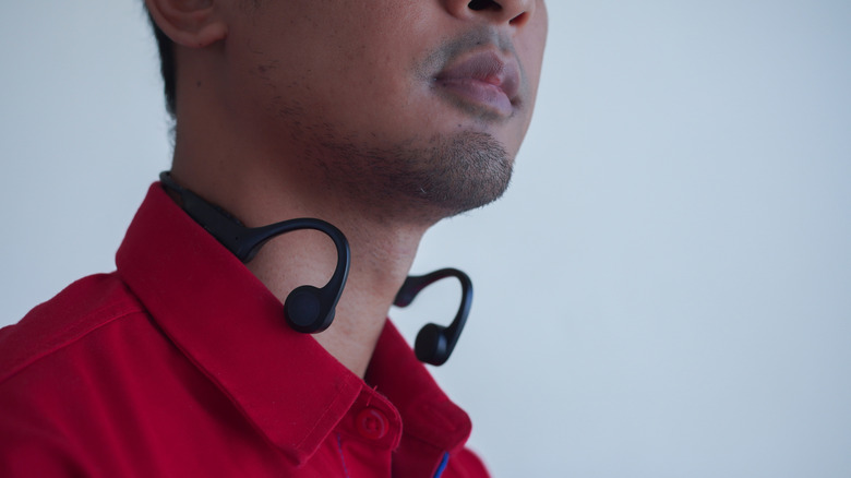 Close-up of a person wearing open-ear bone-conduction headphones around the back of their neck and ears.