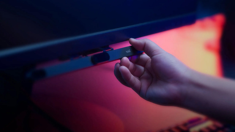 A hand adjusts an eye-tracking sensor attached to the bottom of a monitor.