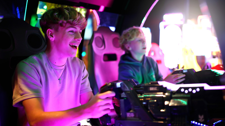A teen and a child play a shooting game in an arcade.