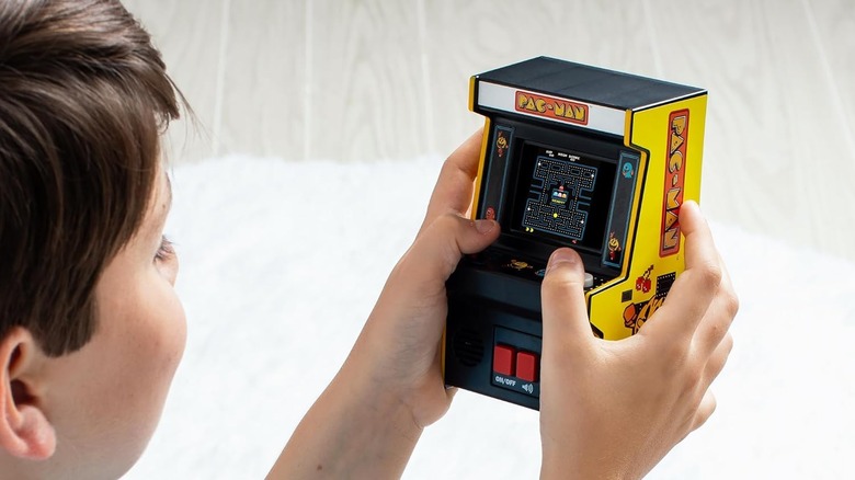 A child playing the Arcade Classics Retro Mini Pac-Man console with a red joystick and color screen.
