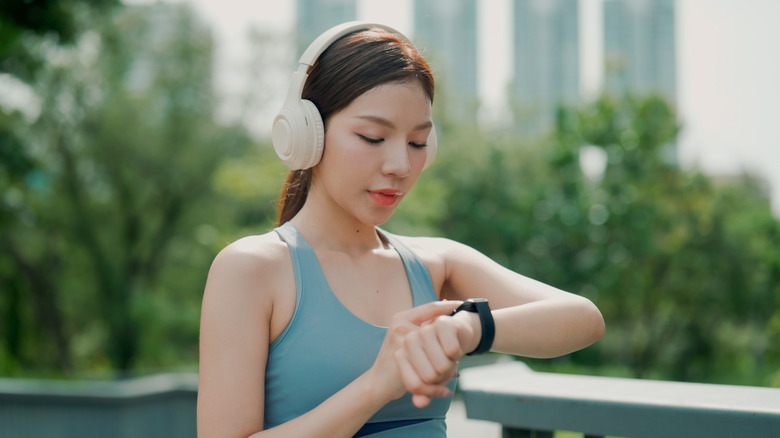 A female runner wearing headphones and looking at a smartwatch on her wrist.